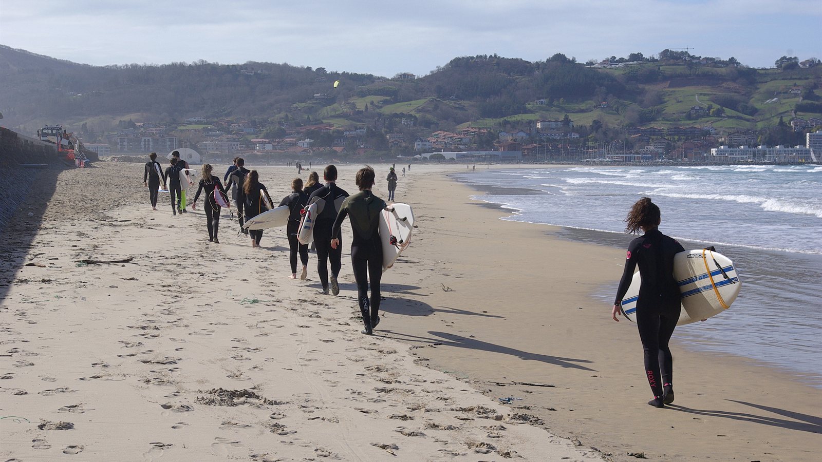 Surf students walking along the beach carrying boards